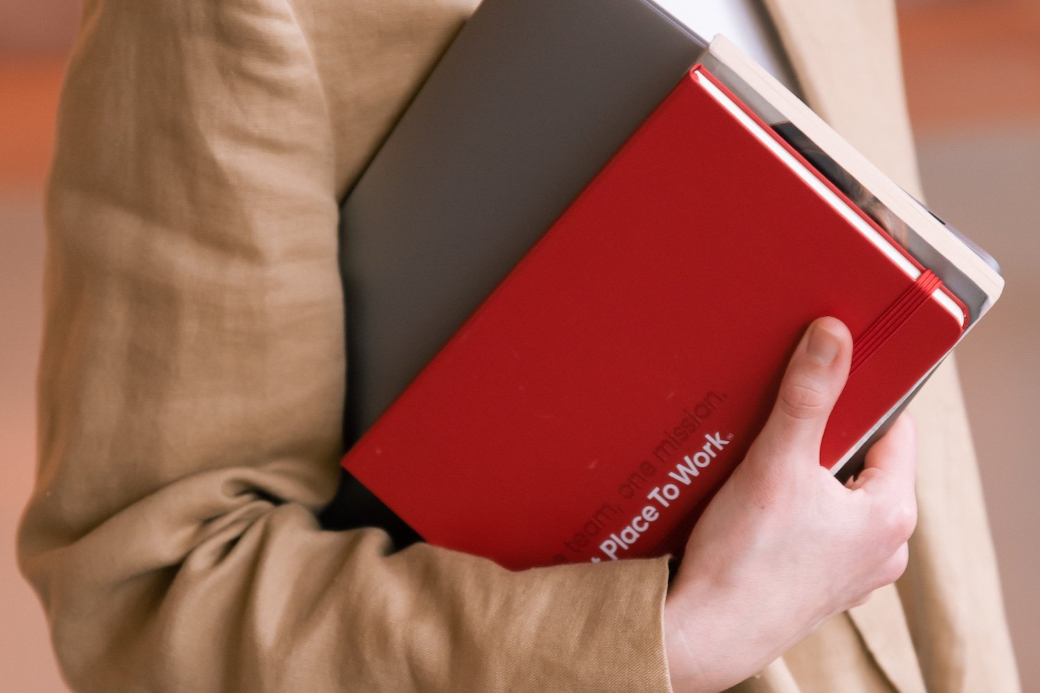 Vrouw houdt laptop en rood notitieboekje van Great Place To Work in haar armen